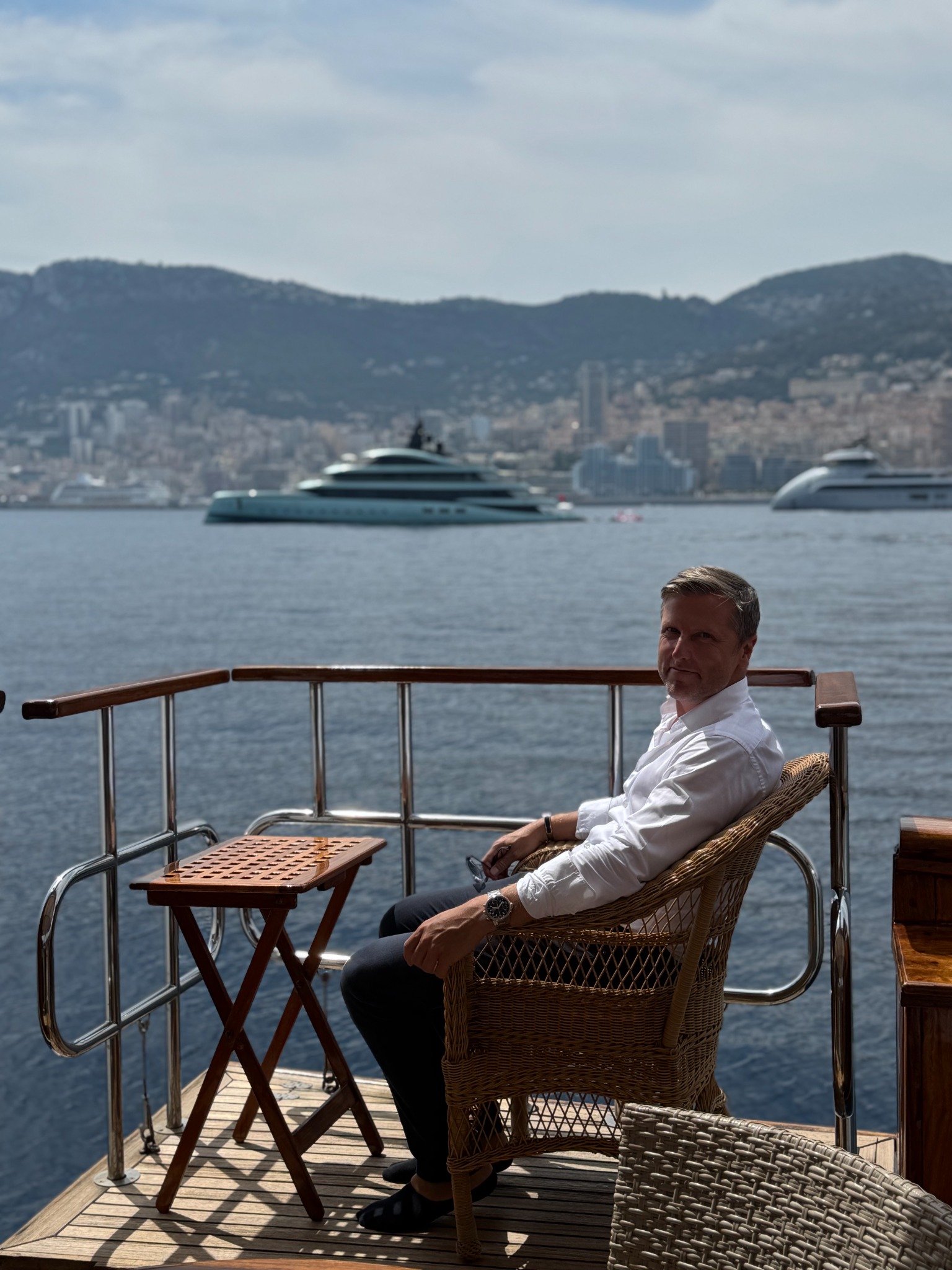 Kenneth Appleyard seated on a yacht with the Riviera coastline behind him